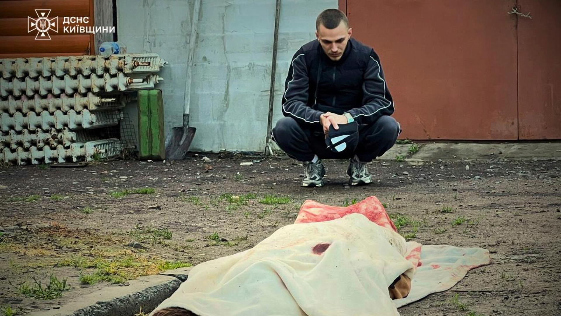 In der Ukraine hockt ein Mann vor einer toten Person. Der Leichnam ist mit einem hellen Tuch abgedeckt. In der Ukraine hockt ein Mann vor einer toten Person. Der Leichnam ist mit einem hellen Tuch abgedeckt.