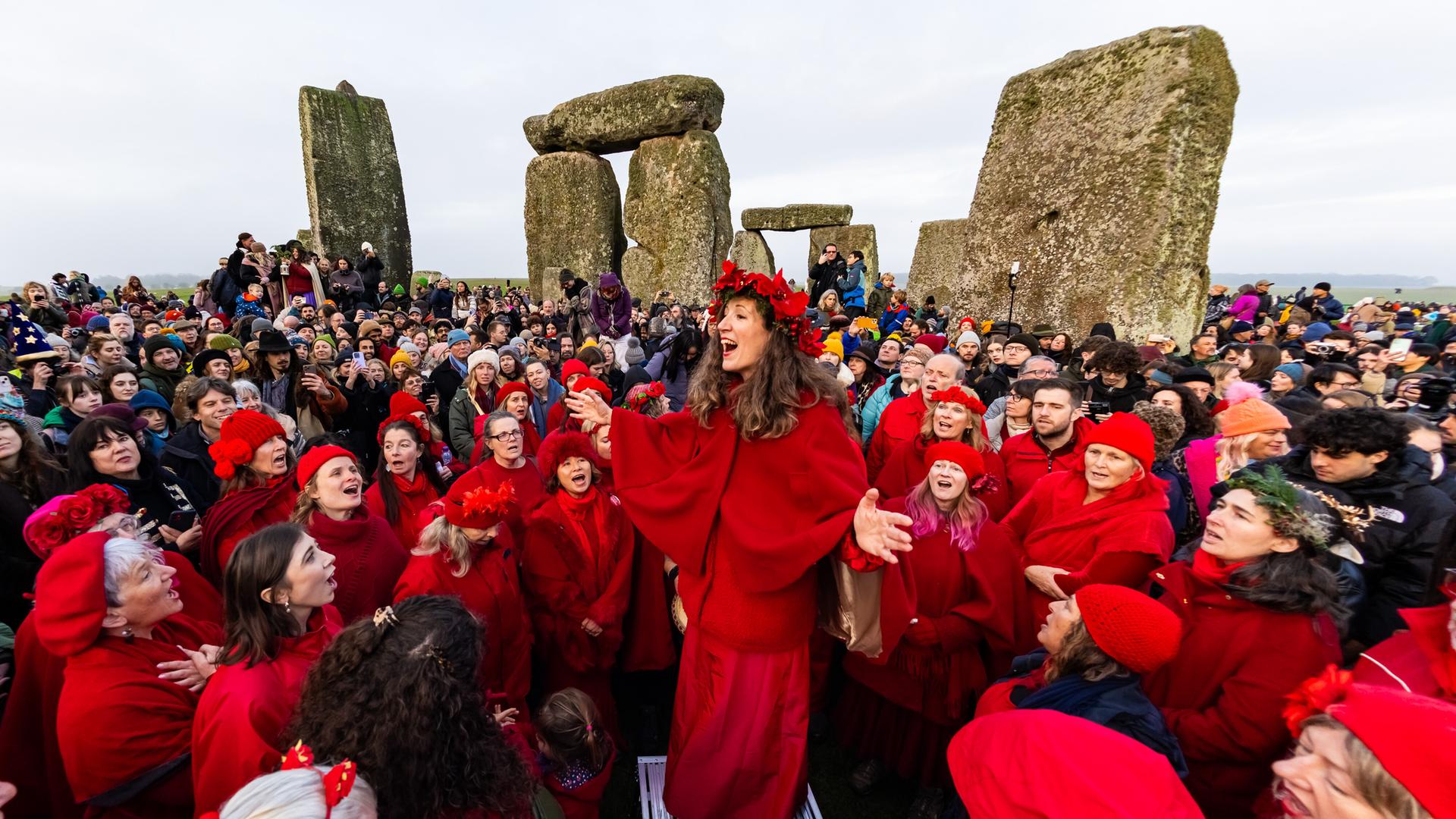Menschen in roten Kostümen und andere feiern vor den Steinen von Stonehenge. 