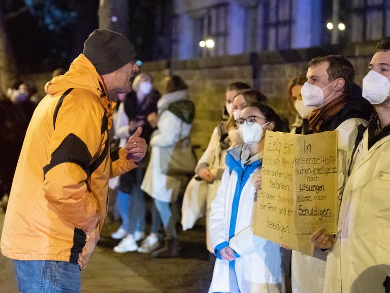 Ein Teilnehmer (l) einer als "Spaziergang" deklarierten Demonstration von Impfgegnern und Kritikern der Corona-Maßnahmen steht vor dem Universitätsklinikum Dresden vor zahlreichen Gegendemonstranten. 