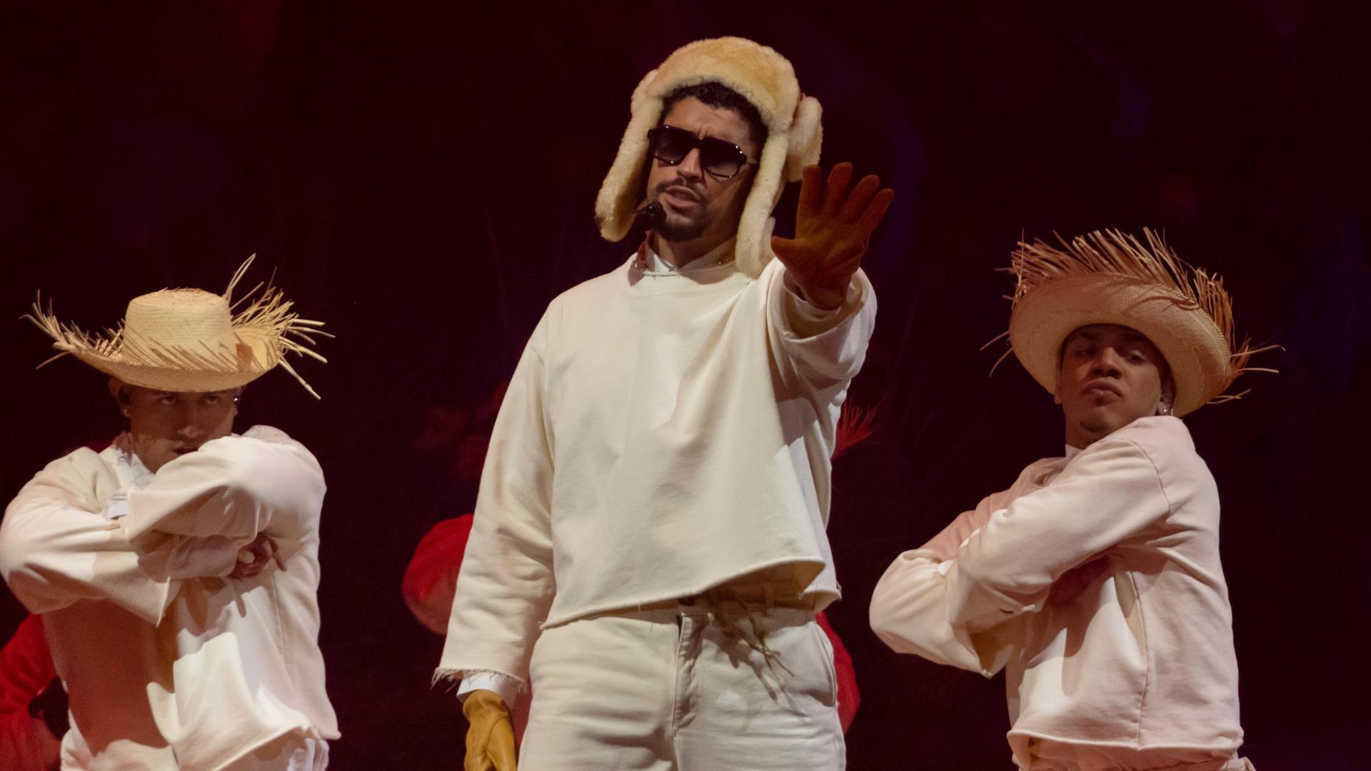 Der Latino-Rapper Bad Bunny trägt eine russische Fellmütze und steht mit zwei Tänzern mit Strohhut auf der Bühne in seiner Heimat Puerto Rico Der Latino-Rapper Bad Bunny trägt eine russische Fellmütze und steht mit zwei Tänzern mit Strohhut auf der Bühne in seiner Heimat Puerto Rico