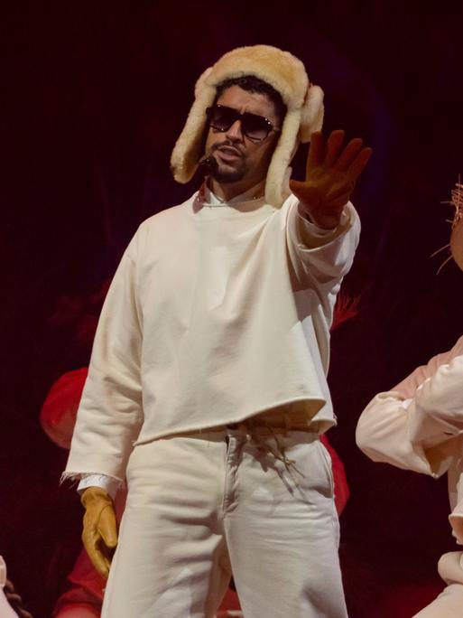 Der Latino-Rapper Bad Bunny trägt eine russische Fellmütze und steht mit zwei Tänzern mit Strohhut auf der Bühne in seiner Heimat Puerto Rico