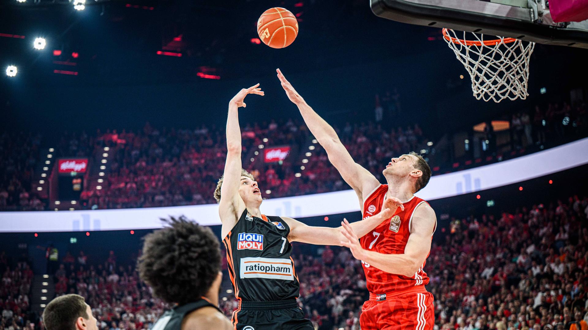 Zwei Spieler steigen vor einem Basketball-Korb zu einem Ball hoch und versuchen beide, ihn als Erste zu erreichen.
