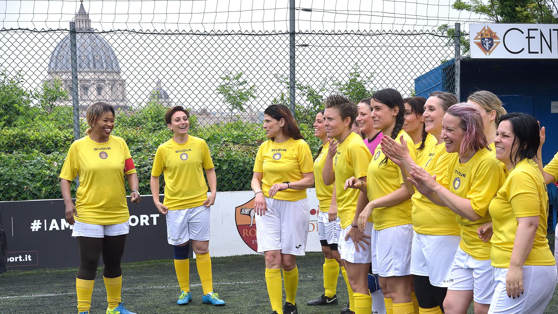 Das Frauen-Fußballteam des Vatikans im Mai 2019. Die Frauen stehen lachend in gelben Trikots und weißen Hosen zusammen. Im Hintergrund ist der Petersdom zu sehen.