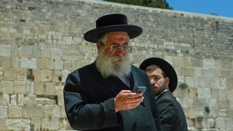 Ein ultraorthodoxer Jude blickt auf sein Mobiltelefon und steht vor der Klagemauer.