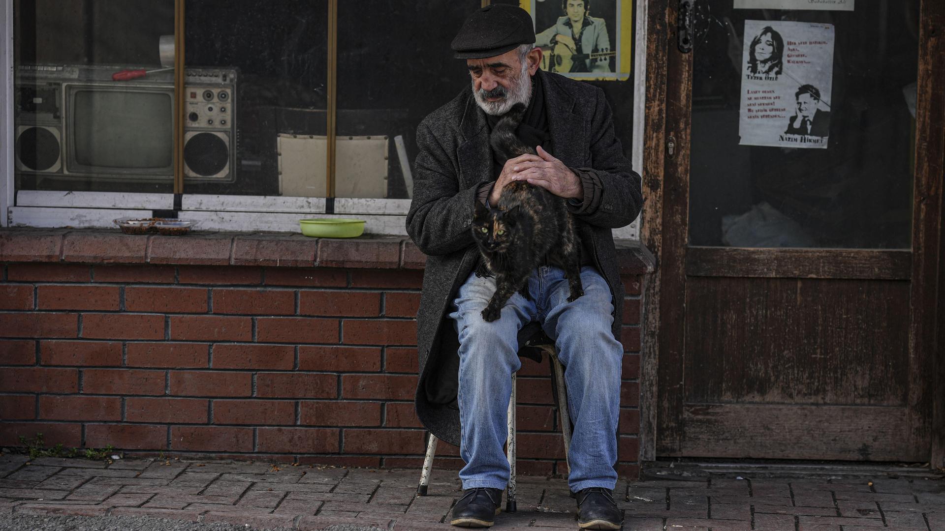 Ein älterer Gebrauchtwarenhändler sitzt in Ankara vor seinem kleinen Laden und streichelt eine Katze auf seinem Schoß. Ein älterer Gebrauchtwarenhändler sitzt in Ankara vor seinem kleinen Laden und streichelt eine Katze auf seinem Schoß.