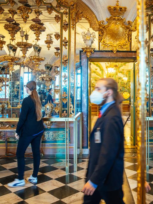 Ein Aufseher und eine Besucherin stehen im Grünen Gewölbe in Dresden vor den prachtvollen Spiegeln und den Vitrinen mit wertvollen Schmuckstücken.