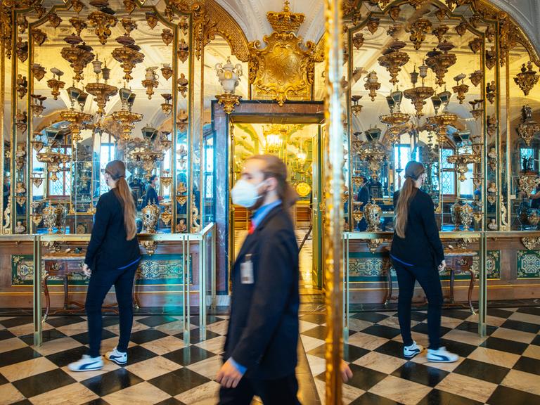 Ein Aufseher und eine Besucherin stehen im Grünen Gewölbe in Dresden vor den prachtvollen Spiegeln und den Vitrinen mit wertvollen Schmuckstücken.