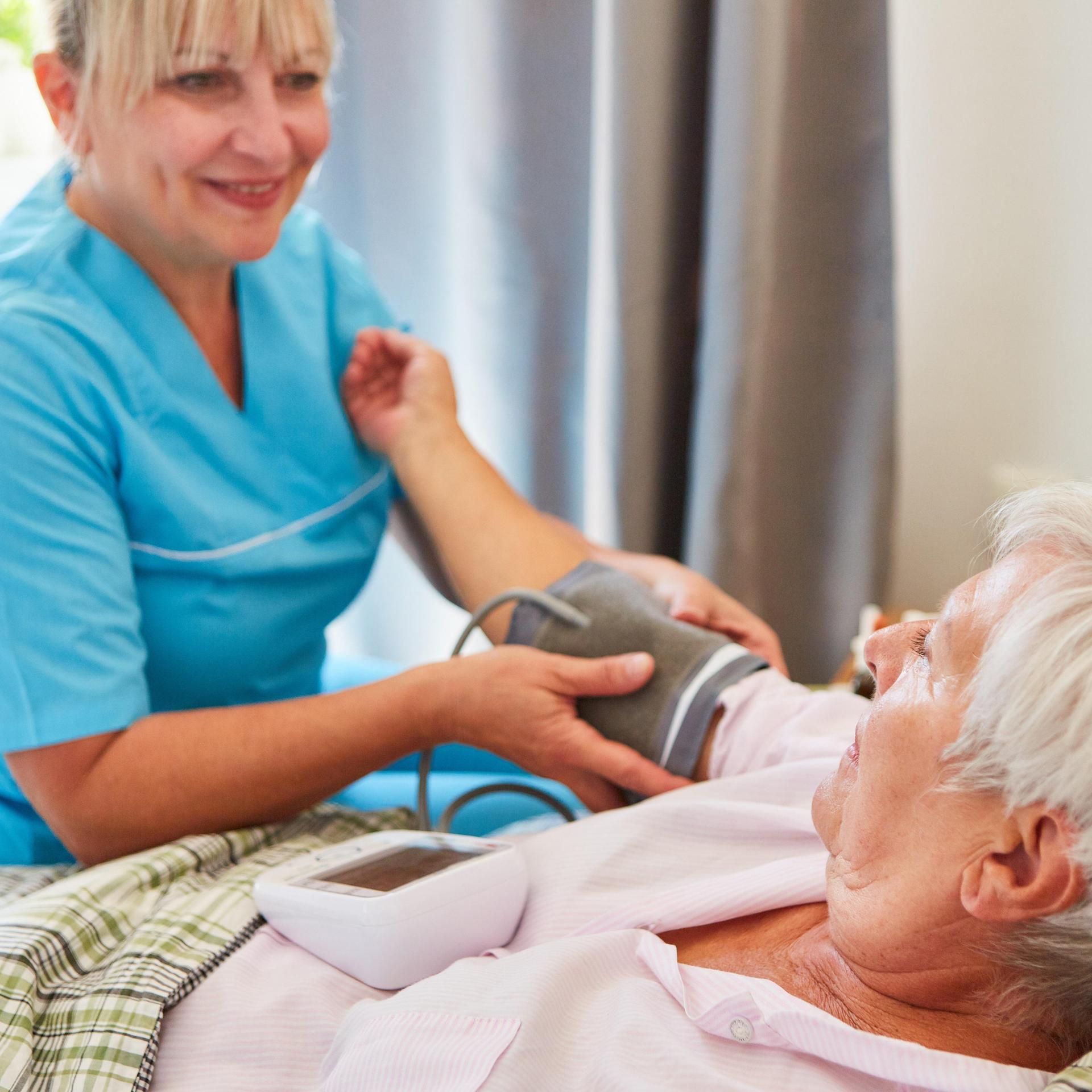 Pflegekraft misst den Blutdruck einer Seniorin zu Hause oder im Pflegeheim