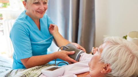 Pflegekraft misst den Blutdruck einer Seniorin zu Hause oder im Pflegeheim.