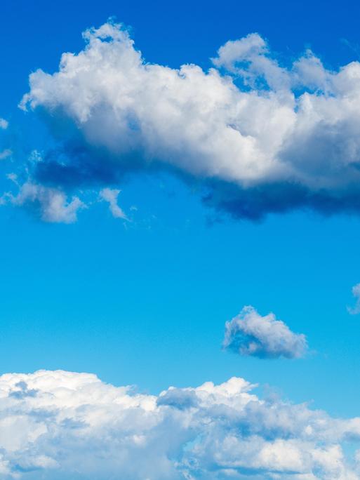 Hellblauer Himmel ist mit weichen kumulierten Wolkenformen gefüllt, darunter ein langes dichtes Wolkenband und verstreut kleinere Wolken in der Entfernung. 