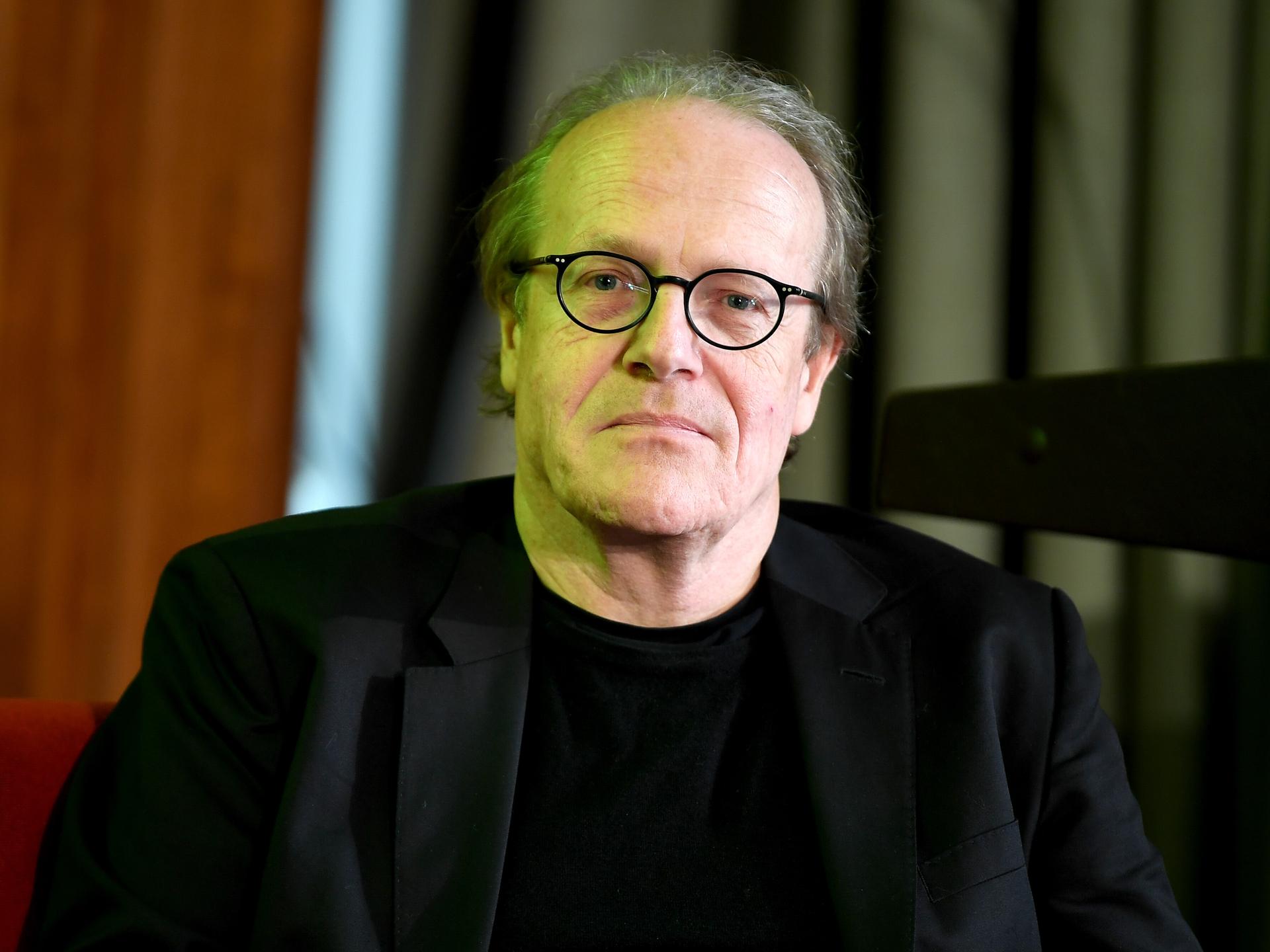 Thomas Flierl schaut direkt in die Kamera. Er trägt ein schwarzes Sakko und eine runde schwarze Brille.