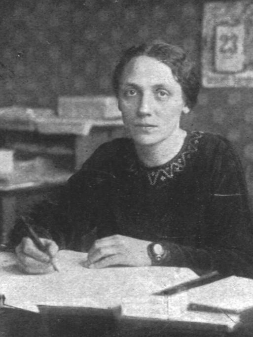 Historisches Schwarzweißfoto einer jungen Frau, die mit ernstem Ausdruck an ihrem Schreibtisch sitzt. Historisches Schwarzweißfoto einer jungen Frau, die mit ernstem Ausdruck an ihrem Schreibtisch sitzt.