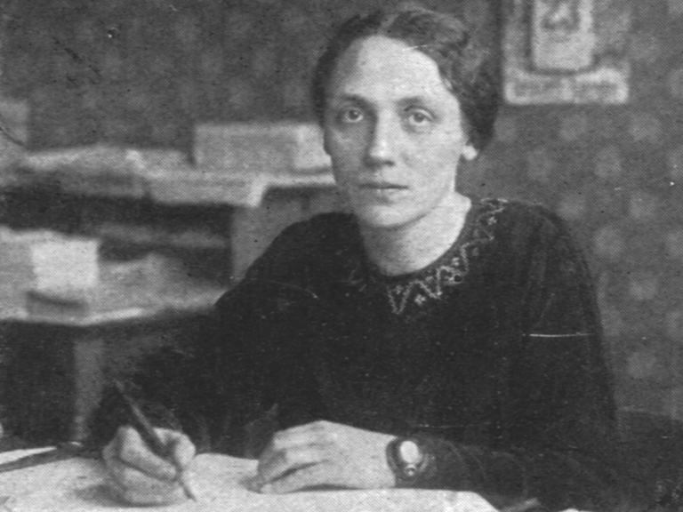 Historisches Schwarzweißfoto einer jungen Frau, die mit ernstem Ausdruck an ihrem Schreibtisch sitzt. Historisches Schwarzweißfoto einer jungen Frau, die mit ernstem Ausdruck an ihrem Schreibtisch sitzt.