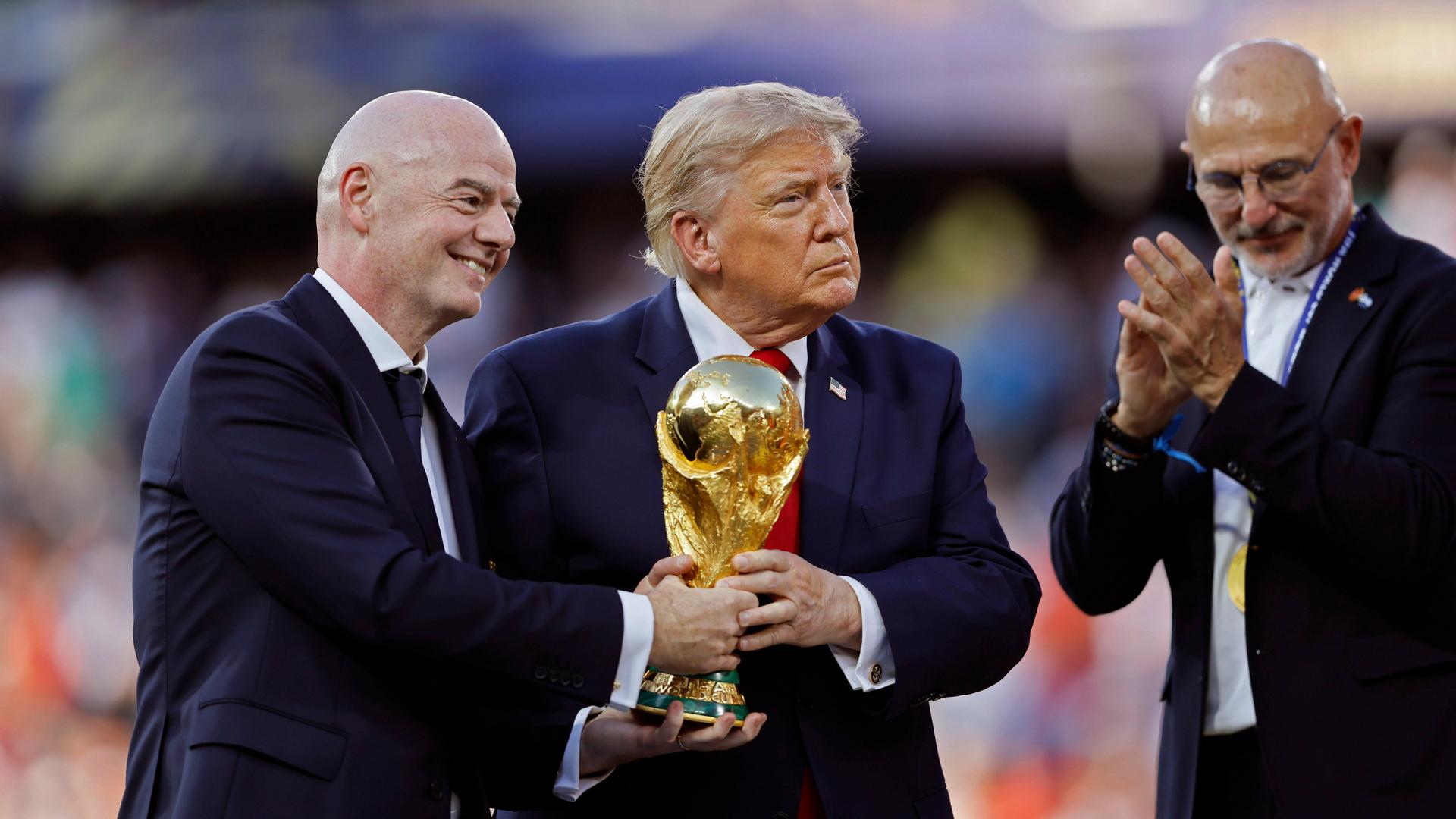 Gianni Infantino und Donald Trump halten bei der Siegerehrung der FIFA WM 2026 den Pokal in Händen, abseits steht der Trainer der siegreichen spanischen Nationalmannschaft Luis de la Fuente. Gianni Infantino und Donald Trump halten bei der Siegerehrung der FIFA WM 2026 den Pokal in Händen, abseits steht der Trainer der siegreichen spanischen Nationalmannschaft Luis de la Fuente.