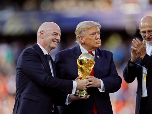 Gianni Infantino und Donald Trump halten bei der Siegerehrung der FIFA WM 2026 den Pokal in Händen, abseits steht der Trainer der siegreichen spanischen Nationalmannschaft Luis de la Fuente.