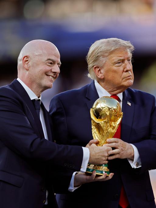 Gianni Infantino und Donald Trump halten bei der Siegerehrung der FIFA WM 2026 den Pokal in Händen, abseits steht der Trainer der siegreichen spanischen Nationalmannschaft Luis de la Fuente.