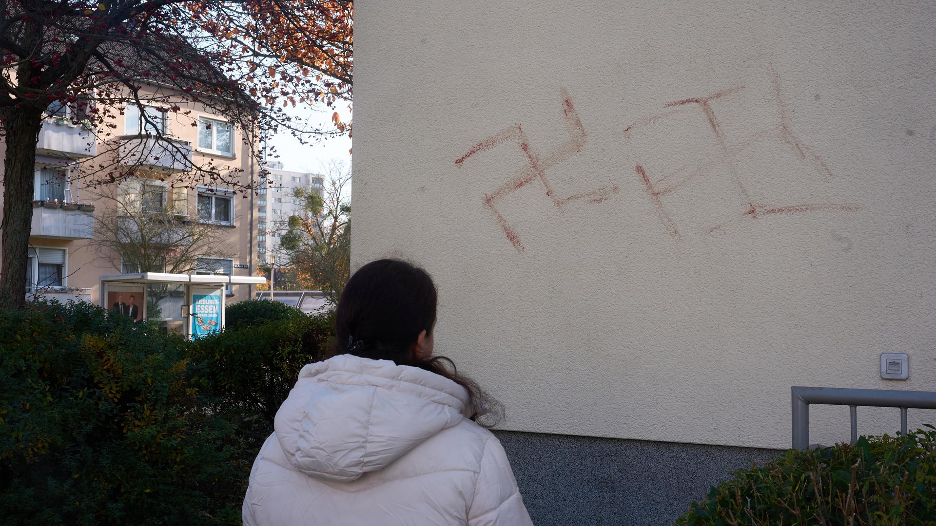 Eine Passantin betrachtet Hakenkreuze, die offensichtlich mit Blut an eine Hauswand geschmiert wurden. 