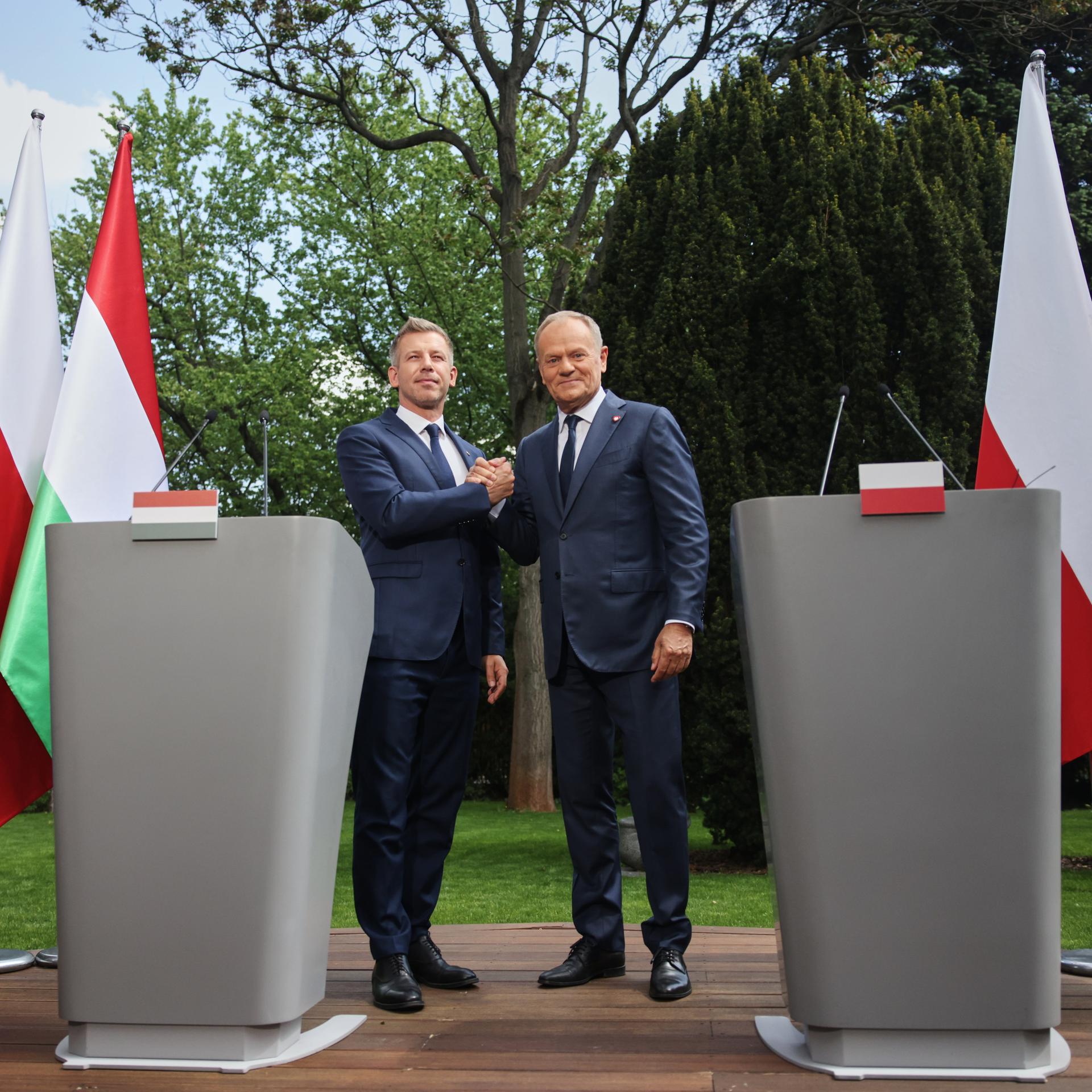 Polens Ministerpräsident Donald Tusk und der ungarische Ministerpräsident Peter Magyar geben sich die Hand. Hinter ihnen jeweils große Landesfahnen und der EU. 