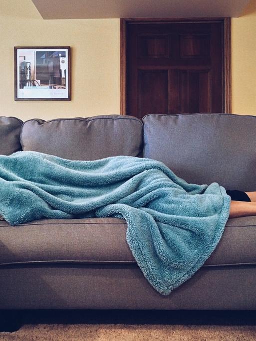 Eine Person liegt unter einer blauen Decke auf dem Sofa