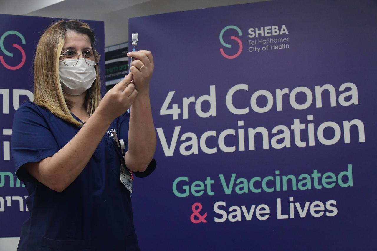 Israel, Ramat Gan: Eine Frau zieht eine Spritze auf, um sie mit Impfstoff zu befüllen. Hinter ihr steht auf einem Plakat: "Vierte Corona-Impfung".