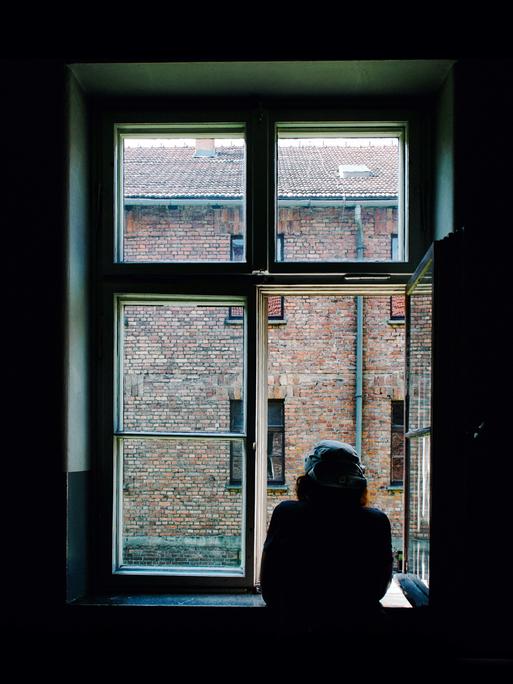 Ein Mann schaut zum Fenster raus in einen Hof. Es herrscht eine ruhige Stimmung.