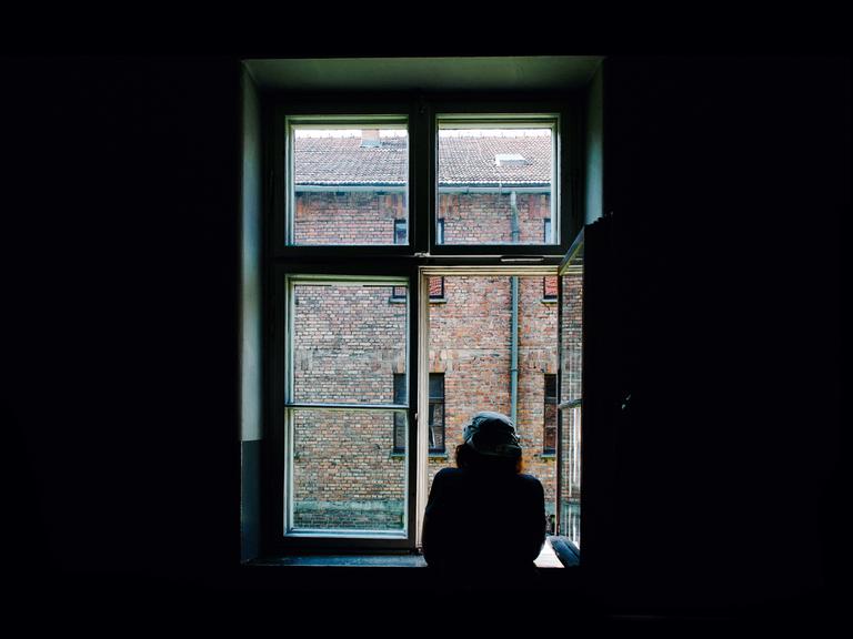 Ein Mann schaut zum Fenster raus in einen Hof. Es herrscht eine ruhige Stimmung.