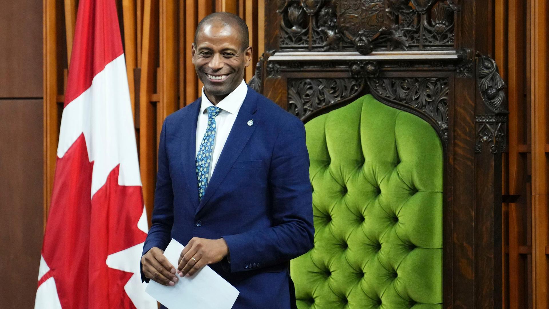 Der neue Vorsitzende im kanadischen Unterhaus, Greg Fergus, lächelt. Er hält ein Papier in der Hand, rechts hinter ihm ist die kanadische Flagge zu sehen. Der neue Vorsitzende im kanadischen Unterhaus, Greg Fergus, lächelt. Er hält ein Papier in der Hand, rechts hinter ihm ist die kanadische Flagge zu sehen.