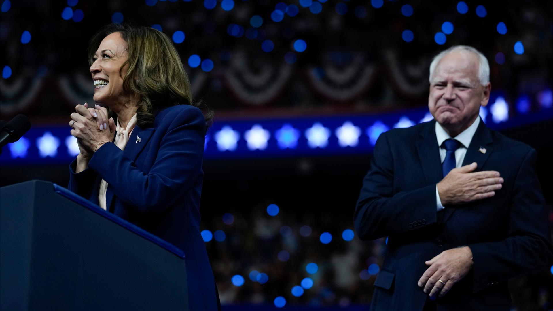 Kamala Harris und Tim Walz jubeln auf einer Wahlkampfbühne ihren Anhängern zu. 