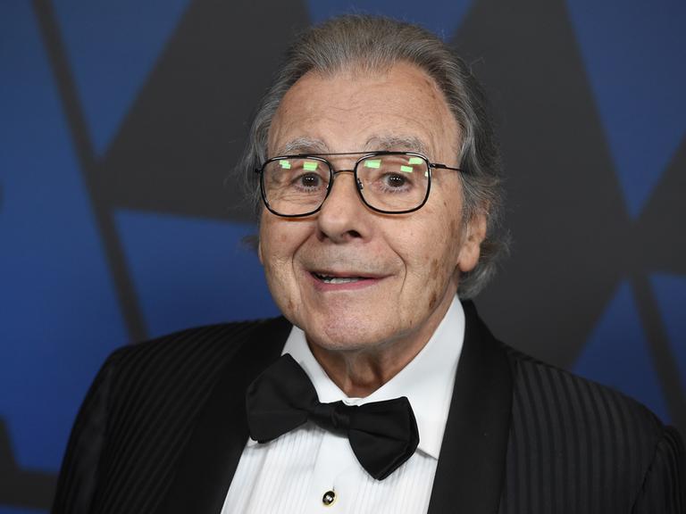 Portrait von Lalo Schifrin, er trägt eine schwarze Fliege, ein schwarzes Sakko und schaut freundlich in die Kamera.