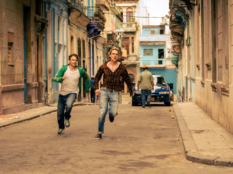 Zwei Männer rennen eine Straße entlang, es scheint in einer Stadt in einem südlichen Land zu sein.