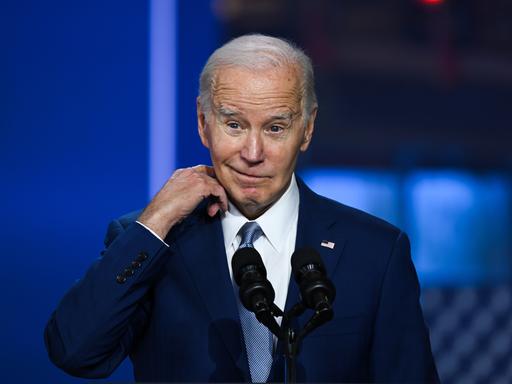 US-Präsident Joe Biden steht auf einer Bühne und schaut skeptisch in die Kamera.