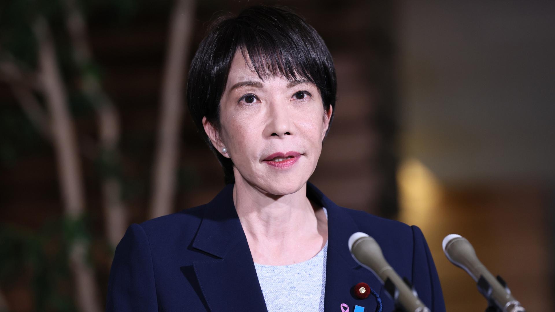 Porträtaufnahme von Japans Premierministerin Takaichi. Vor ihr stehen zwei Mikrofone. Porträtaufnahme von Japans Premierministerin Takaichi. Vor ihr stehen zwei Mikrofone.