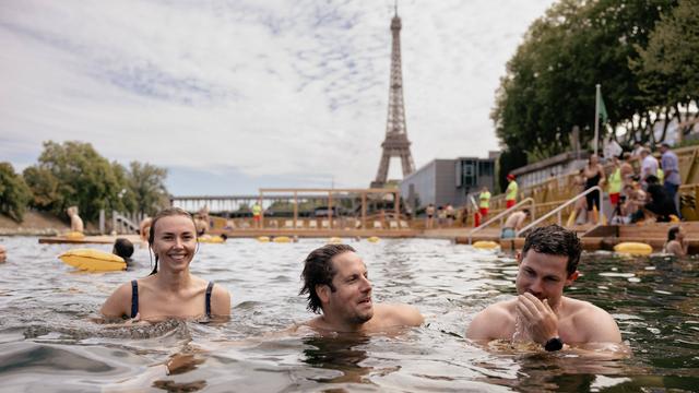 Drei Menschen baden in dem Fluss Seine. Im Hinter-Grund ist der berühmte Eiffelturm zu sehen. 