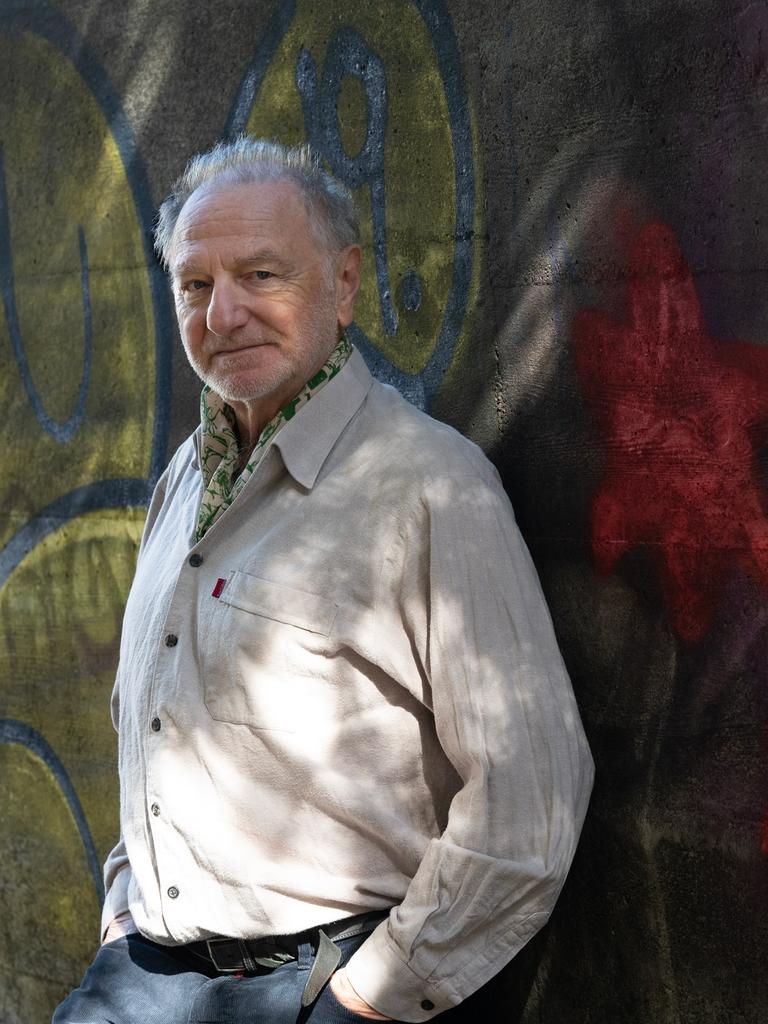 Eric Bergkraut, ein älterer Herr in beigem Leinenhemd und mit kurzem grauem Haar, steht vor einer mit Graffiti bemalten Wand.
