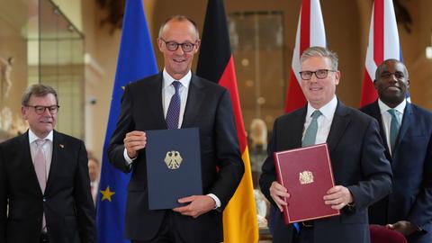 Bundeskanzler Friedrich Merz und Großbritanniens Premier Keir Starmer lächlen in die Kamera. In der Hand halten beide jeweils eine Mappe mit dem so eben unterzeichneten deutsch-britischen Freundschaftsvertrag.