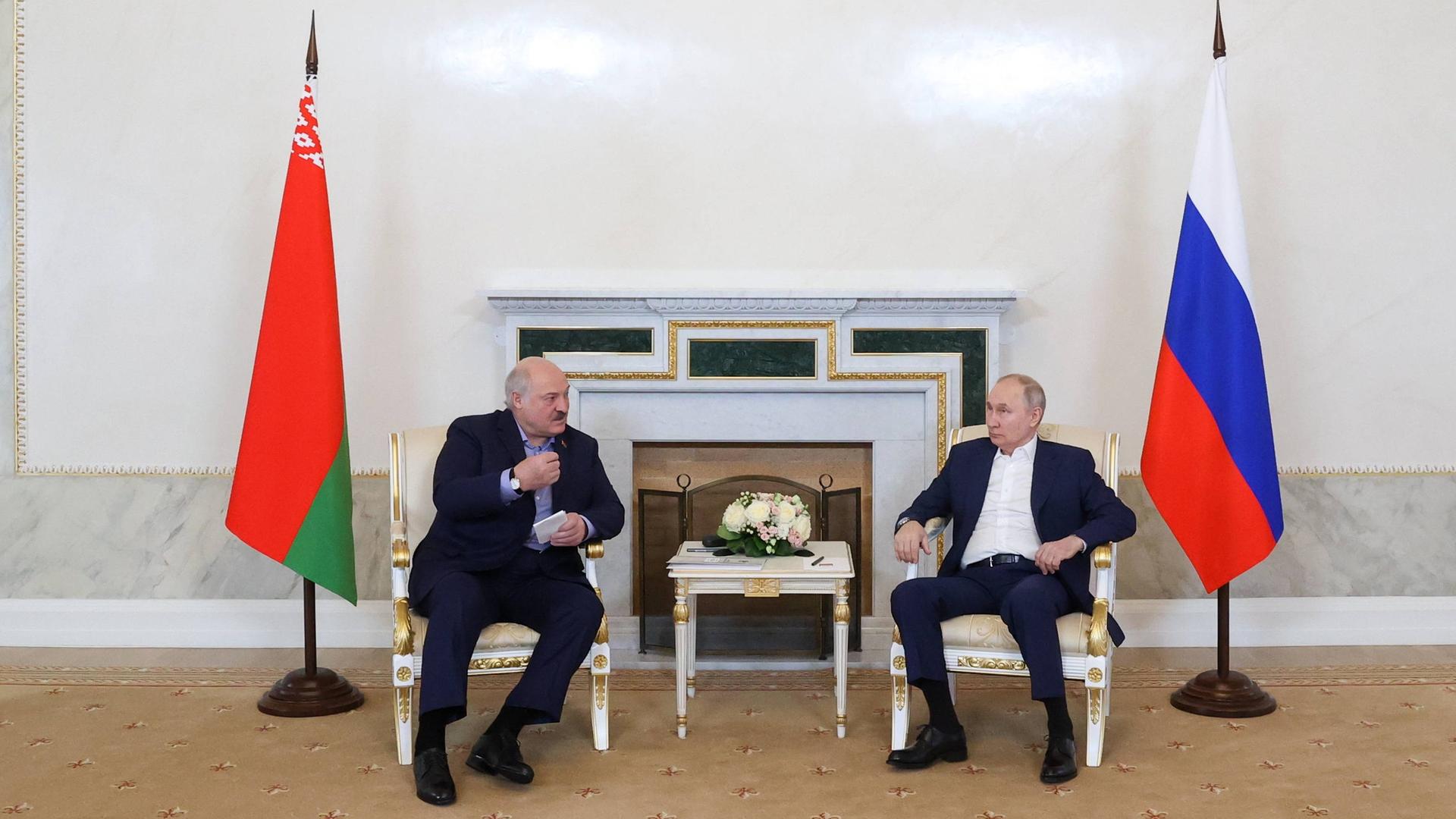 Der Präsident von Belarus Alexander Lukashenko und Russlands Präsident Vladimir Putin gemeinsam an einem Tisch neben ihren Landesflaggen