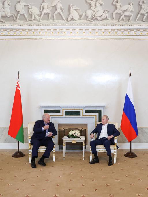 Der Präsident von Belarus Alexander Lukashenko und Russlands Präsident Vladimir Putin gemeinsam an einem Tisch neben ihren Landesflaggen