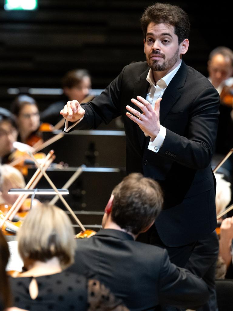 Lahav Shani, zukünftiger Chefdirigent der Münchner Philharmoniker, steht zwischen Musikern auf der Bühne und dirigiert