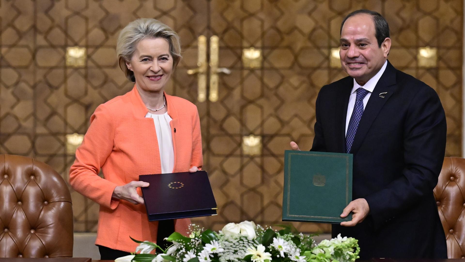 Die Präsidentin der Europäischen Kommission Ursula von der Leyen und der ägyptische Präsident Abdel Fattah al-Sisi bei einem diplomatischen Treffen. Sie halten jeweils eine Mappe in Richtung Kamera. Auf der einen ist das Staatswappen Ägyptens, auf der anderen der Sternenkranz der EU zu sehen.