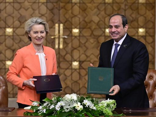 Die Präsidentin der Europäischen Kommission Ursula von der Leyen und der ägyptische Präsident Abdel Fattah al-Sisi bei einem diplomatischen Treffen. Sie halten jeweils eine Mappe in Richtung Kamera. Auf der einen ist das Staatswappen Ägyptens, auf der anderen der Sternenkranz der EU zu sehen.