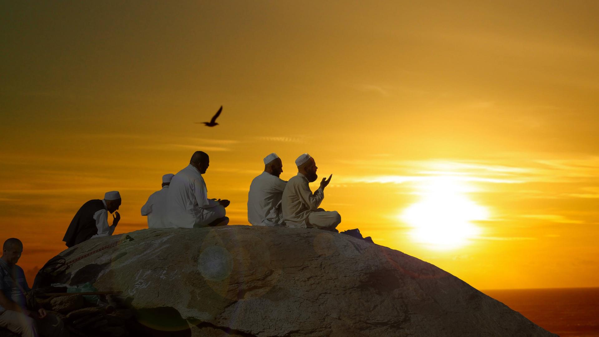 Man sieht ein paar betende Muslime auf dem Berg Arafat. Im Hintergrund geht die Sonne auf. Man sieht ein paar betende Muslime auf dem Berg Arafat. Im Hintergrund geht die Sonne auf.