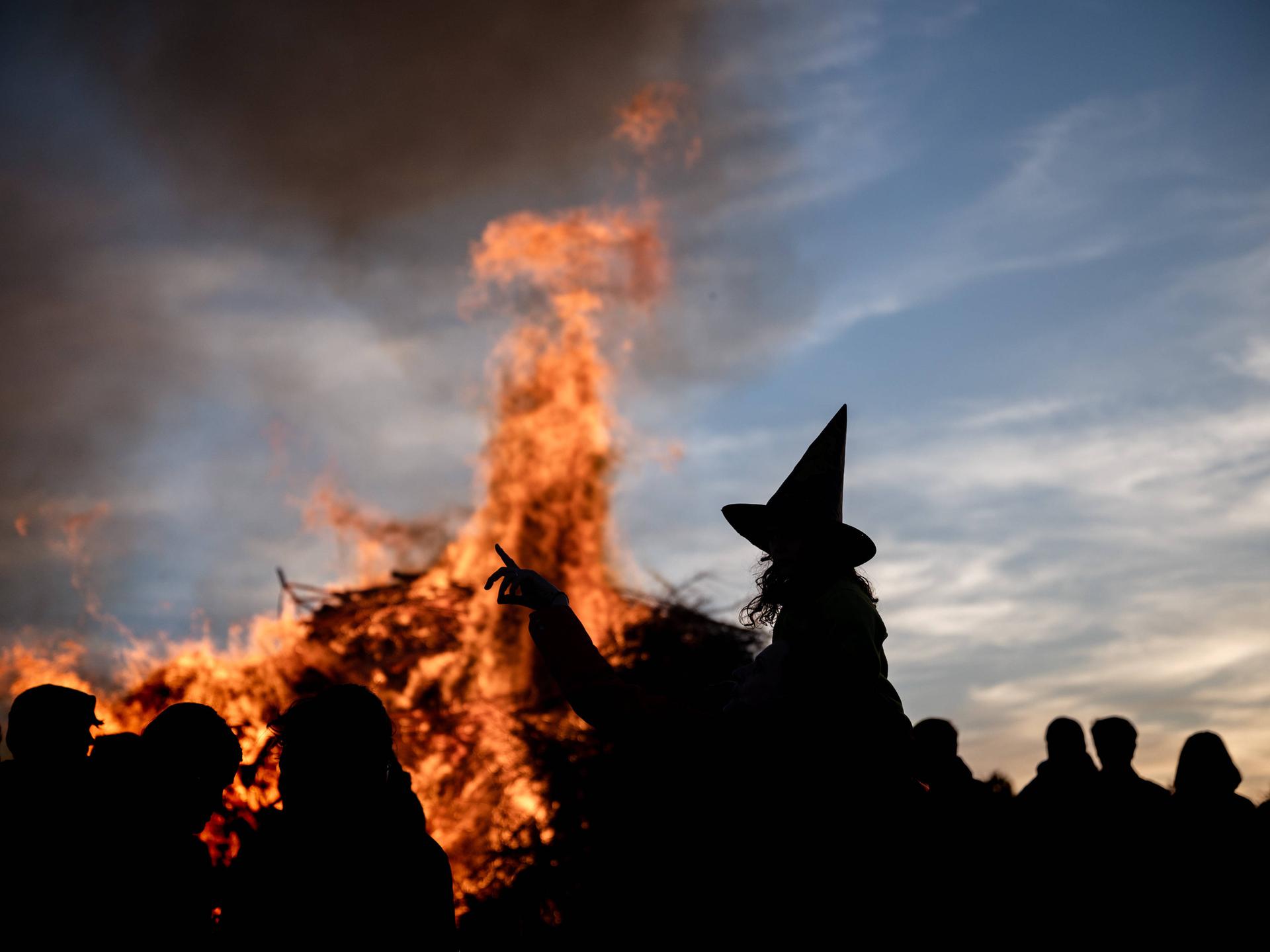 Eine Person als Hexe mit einem Hexenhut zeichnet sich als Silhouette vor einem traditionellen Feuer zur Walpurgisnacht ab