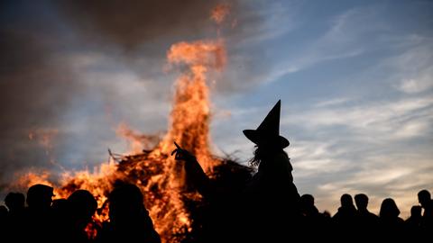 Eine Person als Hexe mit einem Hexenhut zeichnet sich als Silhouette vor einem traditionellen Feuer zur Walpurgisnacht ab