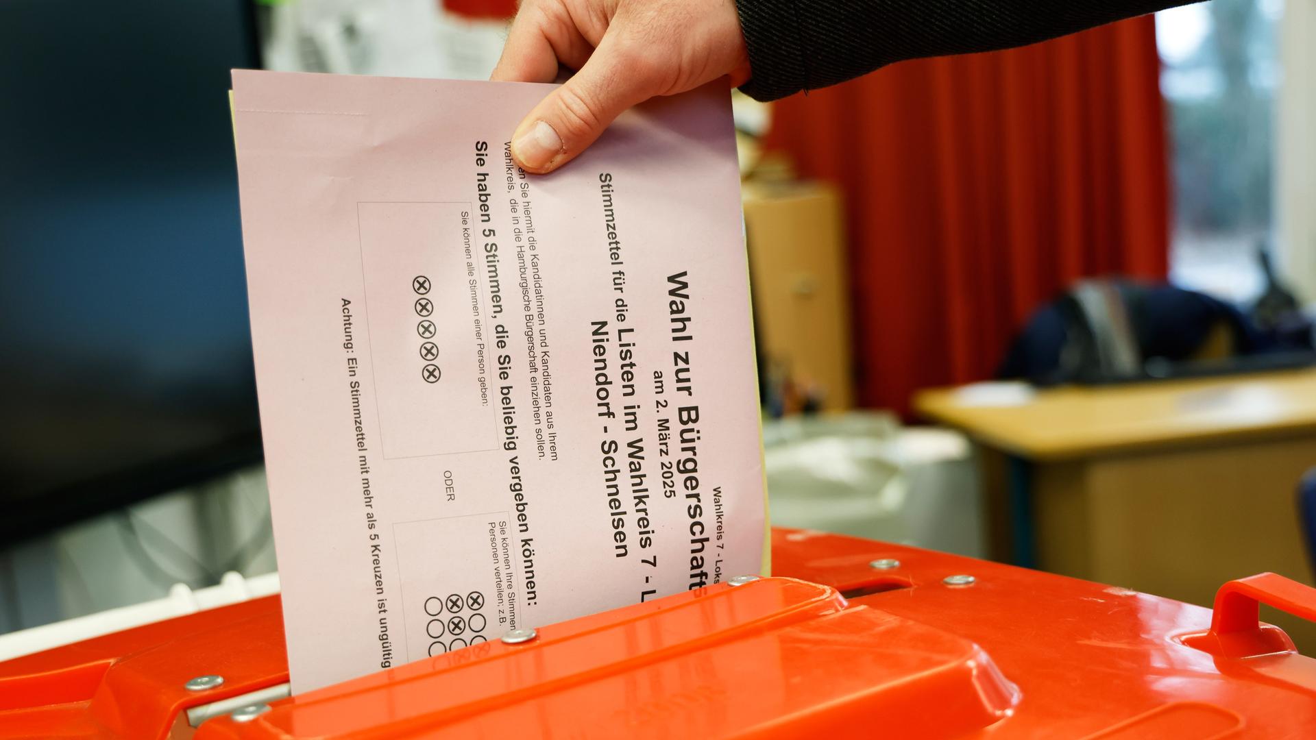 Eine Hand steckt einen Stimmzettel in eine Wahlurne im Wahllokal.