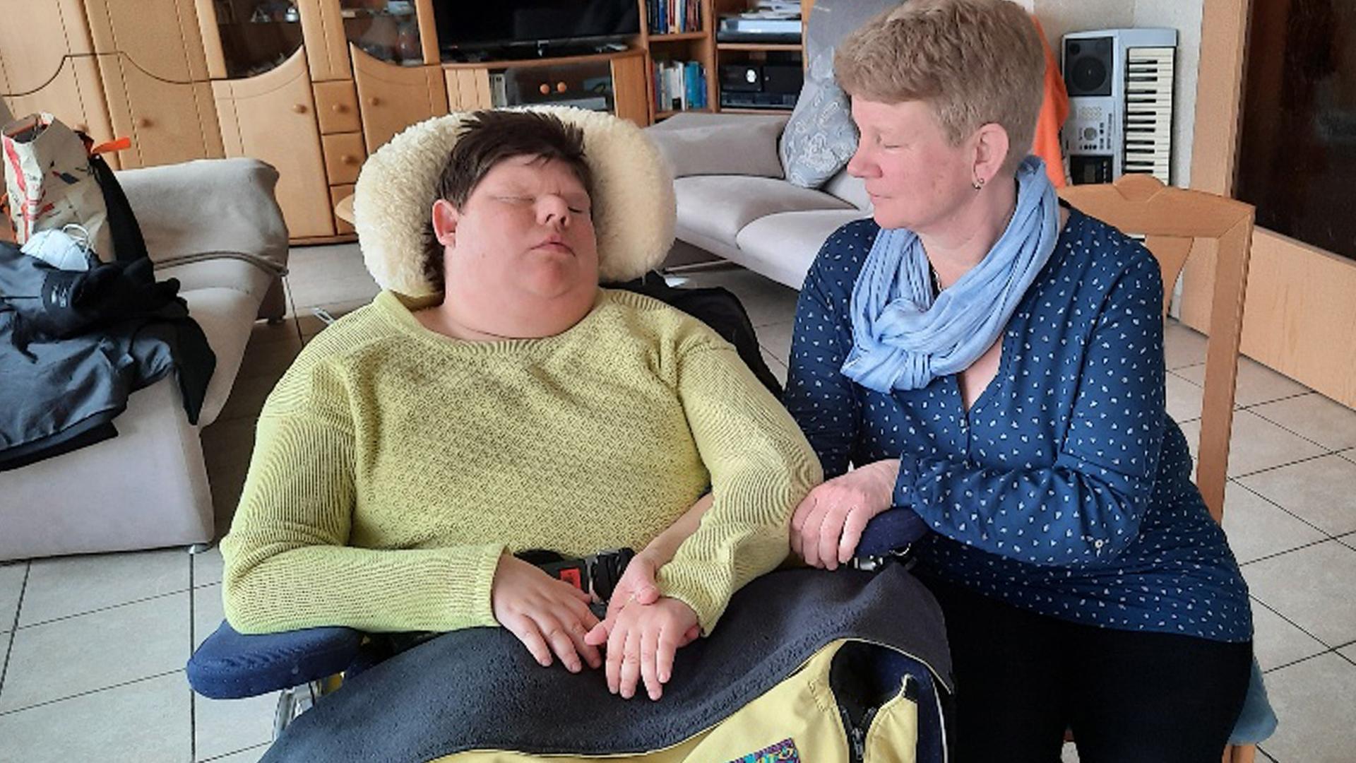 Eine Frau sitzt neben einer jungen Frau, die im Rollstuhl sitzt. 
