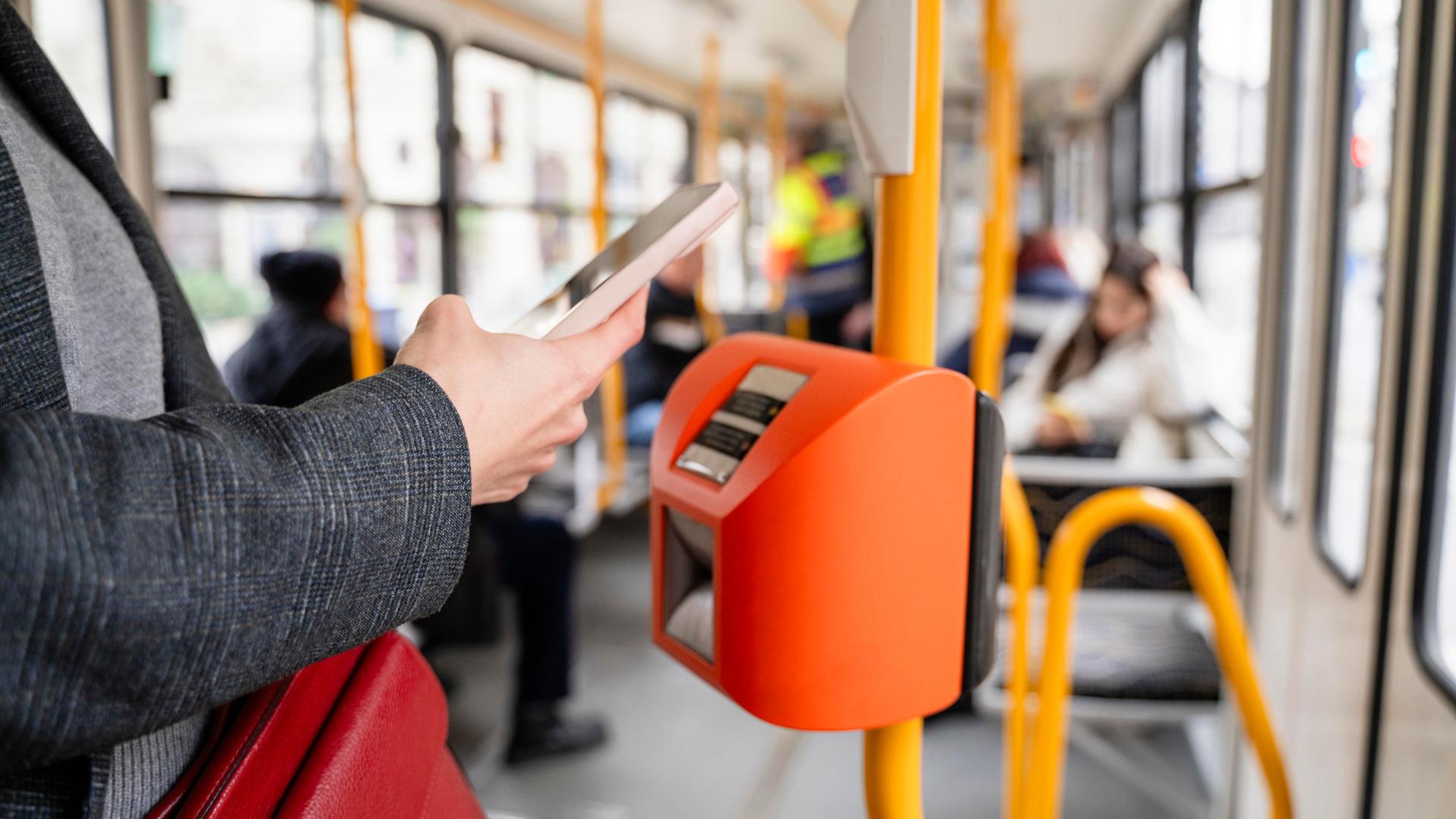 Eine Person bezahlt mit dem Smartphone in einer Straßenbahn.