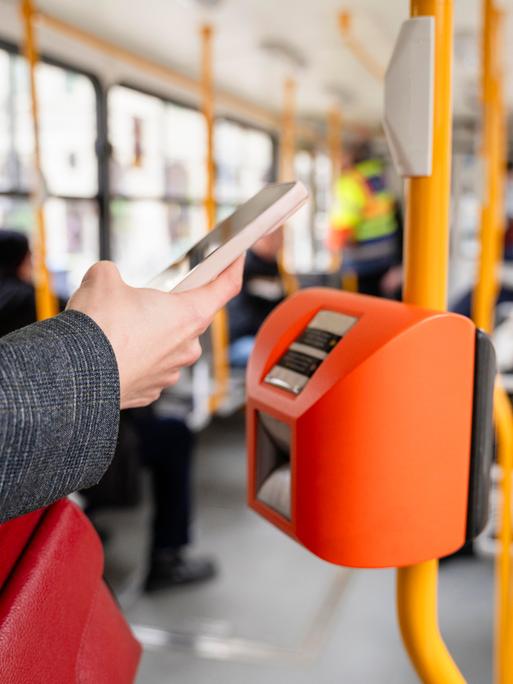 Eine Person bezahlt mit dem Smartphone in einer Straßenbahn.