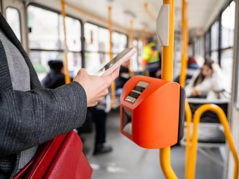 Eine Person bezahlt mit dem Smartphone in einer Straßenbahn.