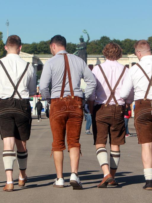 Auftakt zum Oktoberfest in München, Bayern, Deutschland: Männer in Lederhosen spazieren über das Festgelände vor der Bavaria.