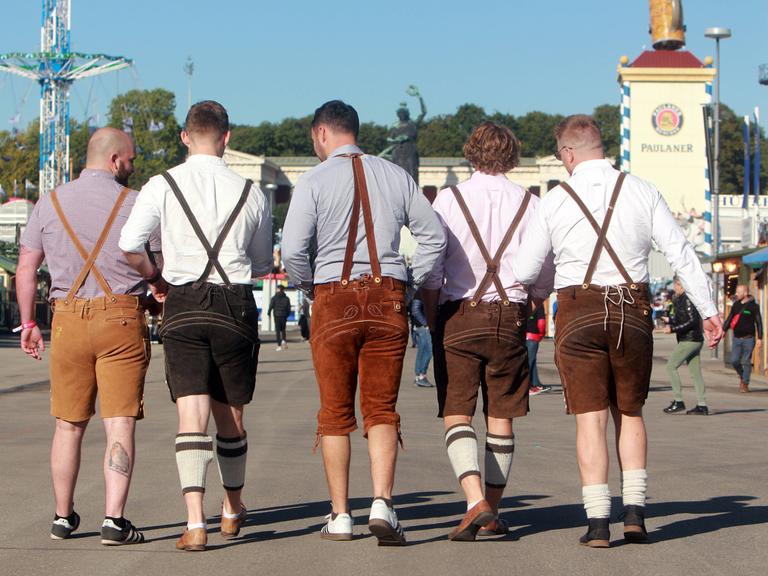 Auftakt zum Oktoberfest in München, Bayern, Deutschland: Männer in Lederhosen spazieren über das Festgelände vor der Bavaria.